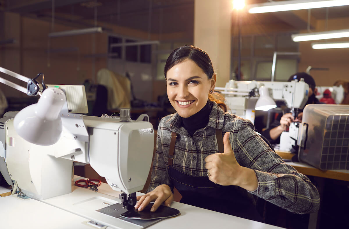 Person using the sewing machine while giving their working conditions a thumbs up